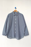 A blue and white conductor striped button up shirt hanging on a wood hanger against a white wall.