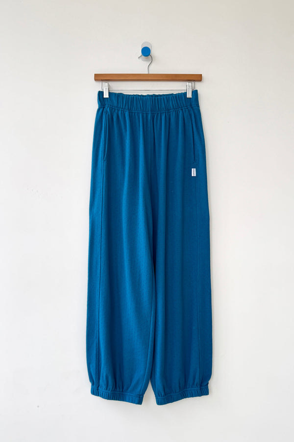 Teal lounge pants hanging on a wooden hanger against a white background
