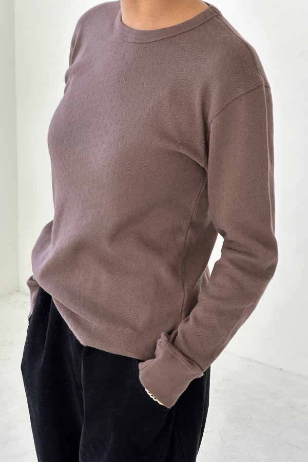 Person wearing a brown long sleeve tee and dark pants against a white background