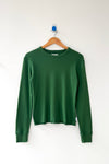 A moss green pointelle knit long sleeve tee hanging on a wood hanger against a white wall.