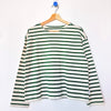 A green and white striped long-sleeve top hanging on a wooden hanger against a plain white wall.