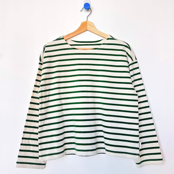 A green and white striped long-sleeve top hanging on a wooden hanger against a plain white wall.