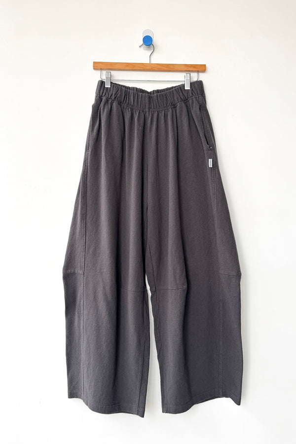 Dark gray wide-leg cotton knit pants with an elastic waistband, hanging from a wooden hanger against a plain white wall.