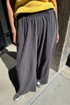 A person wearing loose, wide-leg dark gray pants with an elastic waistband, paired with a yellow top and metallic silver shoes, standing outdoors on a concrete surface.