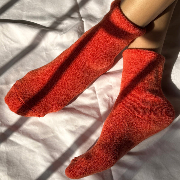 A person wearing a pair of plushy orange-red socks on a white fabric surface.