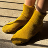 A person wearing a pair of plushy bright olive green socks on a concrete shadowy surface.