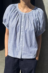 A person wearing a blue and white striped cotton button front top with dark blue jeans.