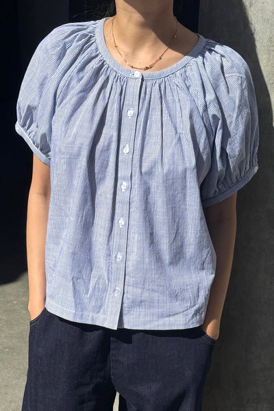 A person wearing a blue and white striped cotton button front top with dark blue jeans.