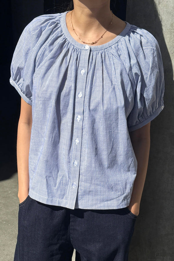 A person wearing a blue and white striped cotton button front top with dark blue jeans.