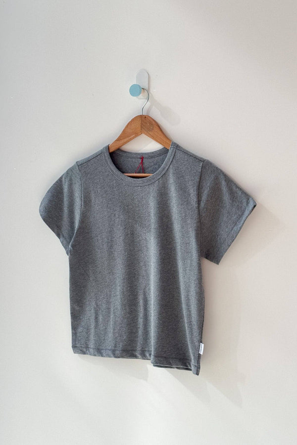 Gray t-shirt on a wooden hanger against a white wall