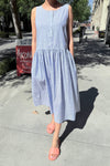 Person wearing a blue and white striped cotton sleeveless dress standing on a city sidewalk. 