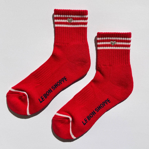 Red socks with white stripes and a silver embroidered heart with 'LE BON SHOPPE' branding on a light gray background