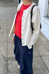 A person standing on a sidewalk wearing a cream-colored snap closure cardigan over a bright red t-shirt, paired with dark navy wide-leg pants and a black shoulder bag.