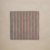 A folded linen napkin featuring a rich striped pattern in dark green, orange, red, and white, with dark red blanket stitching trim against a neutral backdrop.