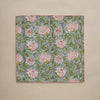 A linen table napkin in a rich blue, green, red, and white floral design with red blanket stitching along the edges, set against a neutral backdrop.