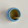 An interior view of a ceramic blue-glazed salt cellar with a small wood spoon, against a neutral backdrop.
