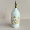 A large ceramic oil pourer with a gold spout. The cylindrical cruet sports a bright white speckled glaze with a floral resist design, allowing the natural clay to show through. The bottle sits against a neutral backdrop.