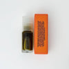 A small roll-on bottle of dark green natural perfume next to its bright orange packaging against a white background.