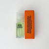 A small clear roll-on bottle of 'Moon Palace', a pale green natural perfume, next to its bright orange packaging box, set against a plain white background.