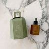 Brown bottle of body oil with dropper and green box on a marble surface