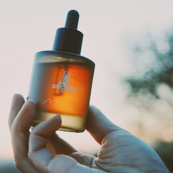 Hand holding a bottle with a dropper against a blurred natural background