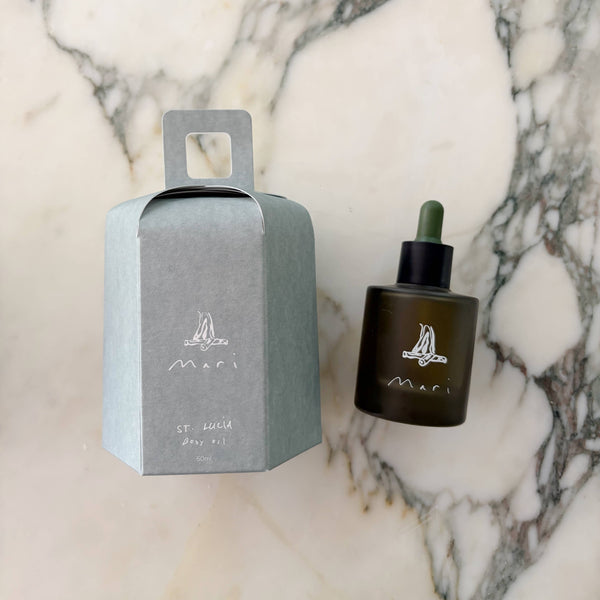 A dark glass oil bottle with dropper and light blue paper packaging on a marble surface.