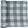 A partially unrolled muslin swaddle blanket in a tonal dusty blue large gingham print on a white backdrop. 