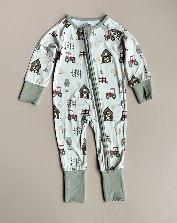 A baby zip-front romper in white with farm motifs and light green trim & cuffs against a neutral backdrop.