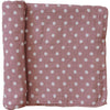 A partially unrolled muslin swaddle blanket in a dusty pink with white polka dots against a white backdrop.