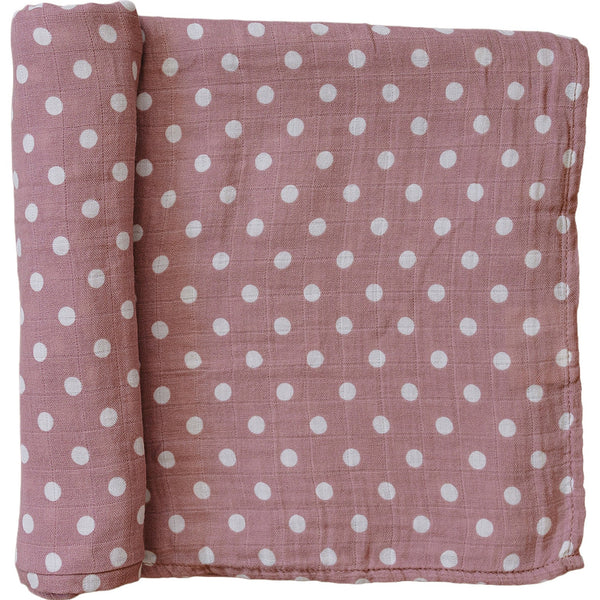 A partially unrolled muslin swaddle blanket in a dusty pink with white polka dots against a white backdrop.