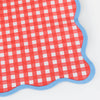 Close up detail of a red and white checkered paper napkin with blue wavy border on a white background