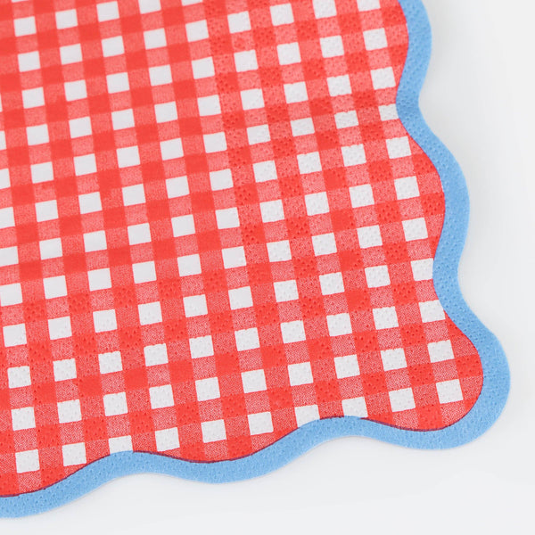 Close up detail of a red and white checkered paper napkin with blue wavy border on a white background
