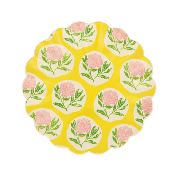 Round yellow small plate with pink, green and white floral design and wavy edge on a white background