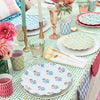 Colorful table setting with floral plates, glasses, and cutlery on a patterned tablecloth.