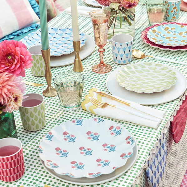 Colorful table setting with floral plates, glasses, and cutlery on a patterned tablecloth.