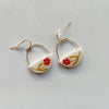 Glossy ivory polymer clay earrings in a half circle shape, painted with a red and chartreuse floral design hanging from gold wire arches and gold hooks on a neutral background.