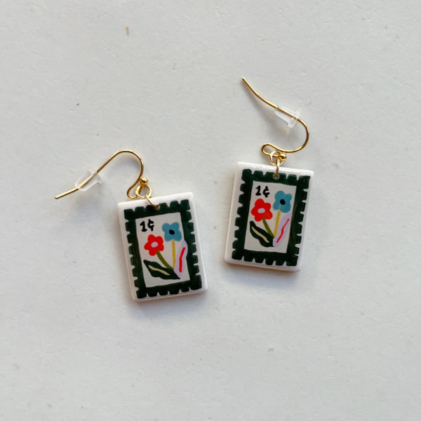 Colorful polymer clay earrings hand painted in a floral 1 cent postage stamp design with gold hooks on a neutral background.