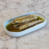A white dish with mackerel fillets in oil on a marble countertop.