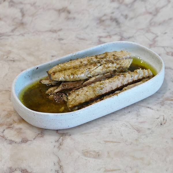 A white dish with mackerel fillets in oil on a marble countertop.