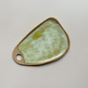 A ceramic serving board with a circular cutout handle and swirling golden yellow and off-white speckly glaze in an oblong wedge shape against a neutral backdrop.