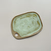 A ceramic serving board with a circular cutout handle and swirling golden yellow and off-white speckly glaze in an oblong rectangular shape against a neutral backdrop.
