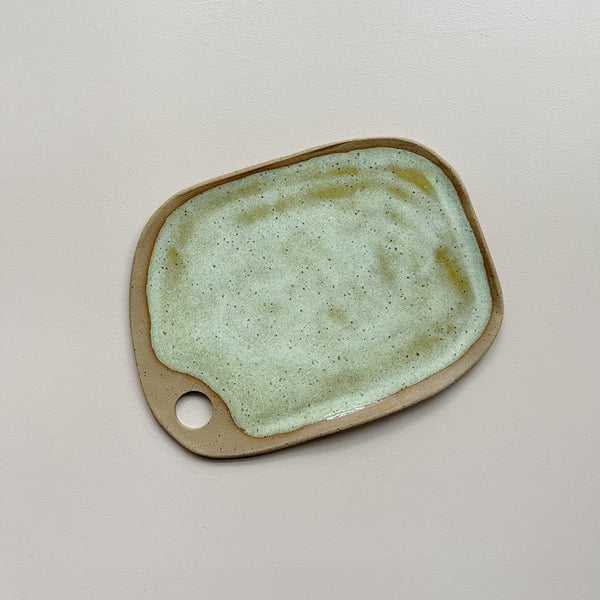 A ceramic serving board with a circular cutout handle and swirling golden yellow and off-white speckly glaze in an oblong rectangular shape against a neutral backdrop.