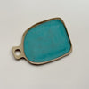 A ceramic serving board with a circular cutout handle and a vibrant teal speckled glaze in an oblong shape against a neutral backdrop.