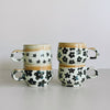 Two stacks of ceramic mugs, featuring a variety of off-white and black floral glaze designs.