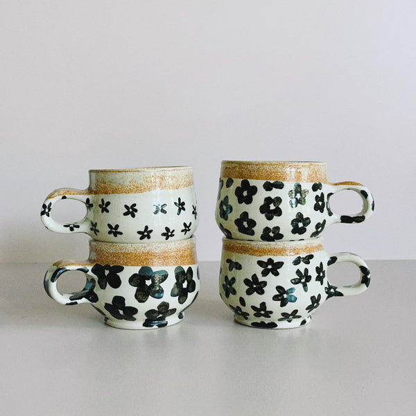 Two stacks of ceramic mugs, featuring a variety of off-white and black floral glaze designs.
