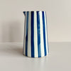 A ceramic handle-less pitcher jug in bold navy blue and natural white stripes against a neutral backdrop.