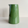 A ceramic handleless pitcher jug featuring a vibrant moss green and narrow white striped pattern, sitting against a neutral backdrop.