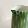 A close up view of the pour spout on a green and white striped ceramic pitcher jug, against a neutral backdrop.