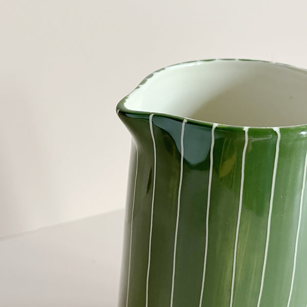 A close up view of the pour spout on a green and white striped ceramic pitcher jug, against a neutral backdrop.