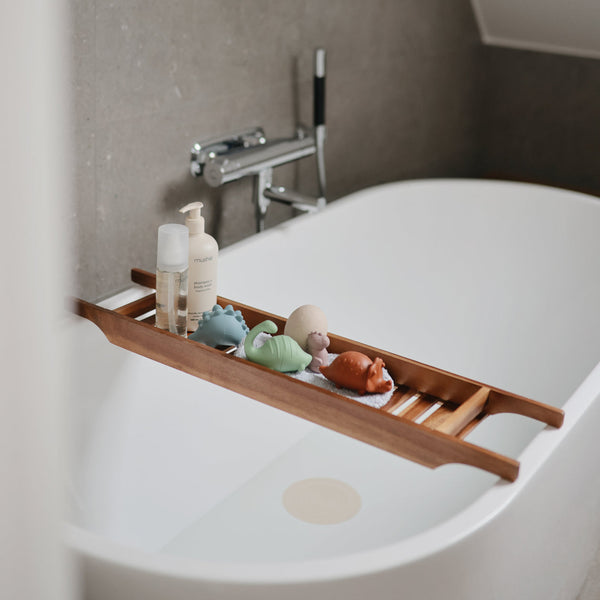 Wooden bath tray with bath products and toys on a white bathtub